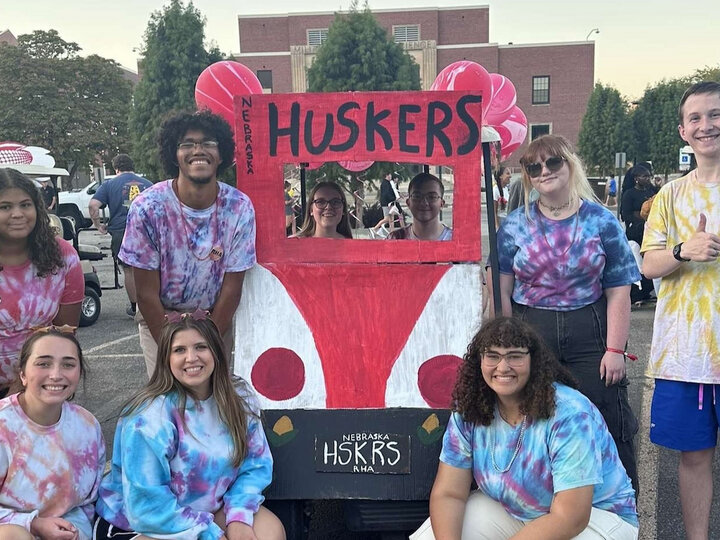 Student posing in front of "Huskers" golf cart for Homecoming.